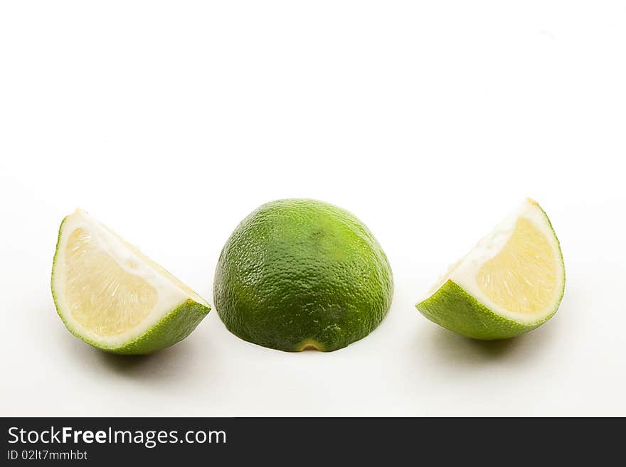 Two lime sections pulp on either side of a face down half with rind showing on white background. Two lime sections pulp on either side of a face down half with rind showing on white background.