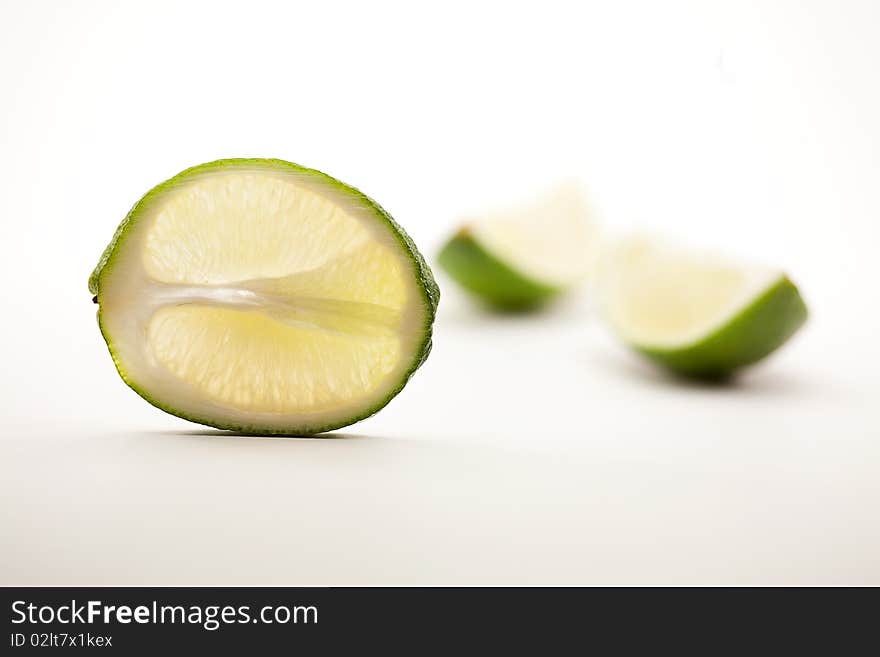 One lime slice standing vertically upright with two quarter lime segments out of focus on white background. One lime slice standing vertically upright with two quarter lime segments out of focus on white background