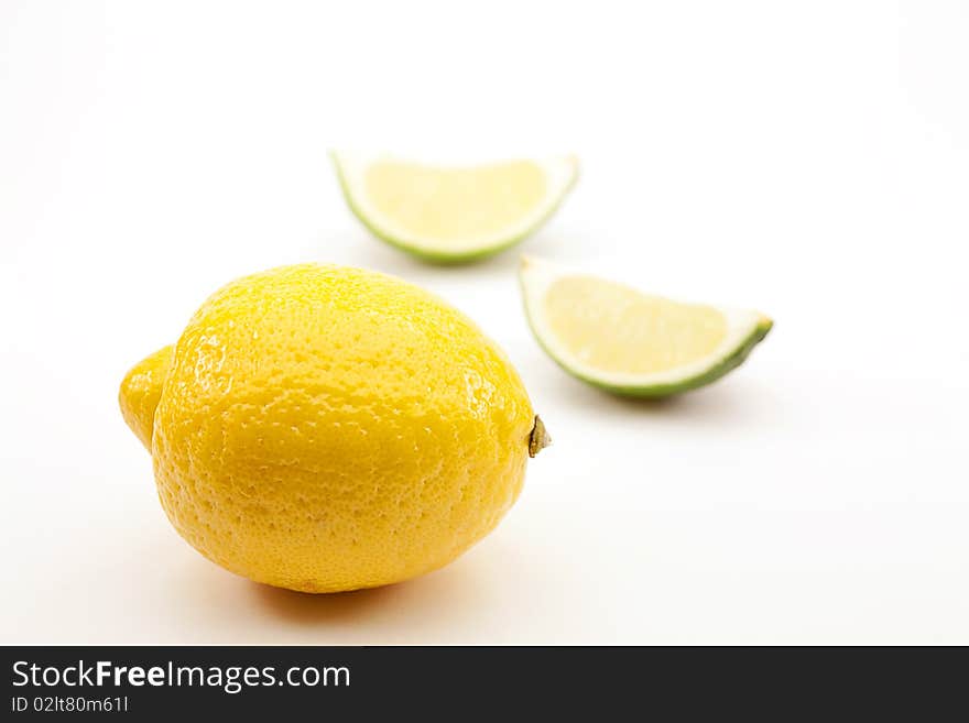 One whole lemon and two out of focus lime sections on white background. One whole lemon and two out of focus lime sections on white background.