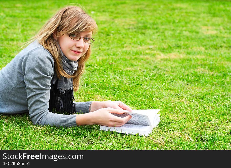 The girl lays on a green grass, and reads the book. The girl lays on a green grass, and reads the book