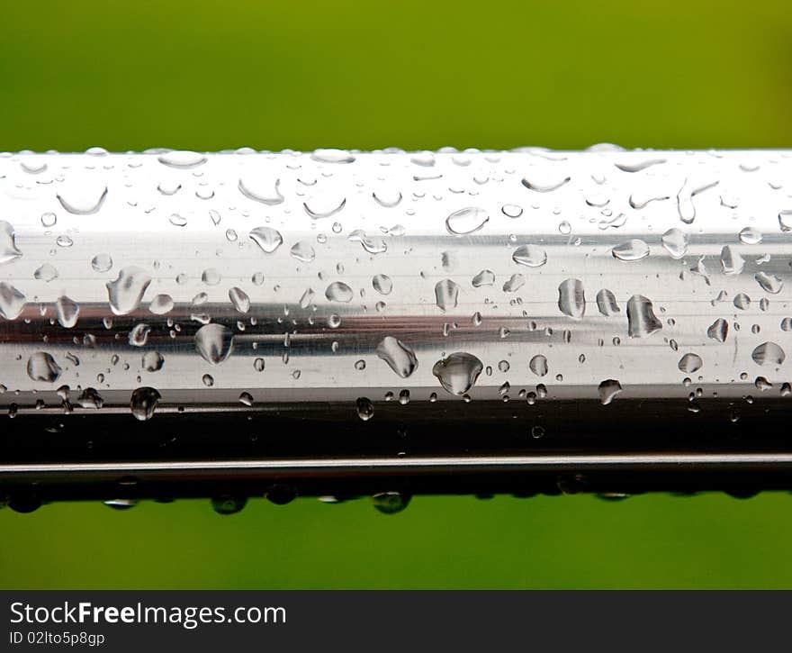 Rain drops on chrome surface on green background