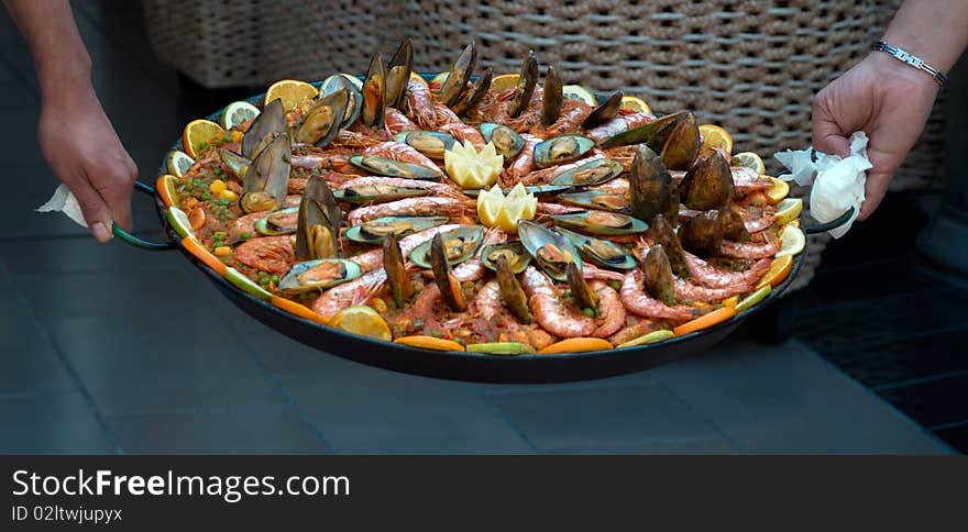 Two men holding a large dish of seafood paella