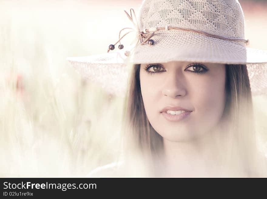 Young beautiful girl with hat staring at camera among green wheat. Young beautiful girl with hat staring at camera among green wheat.