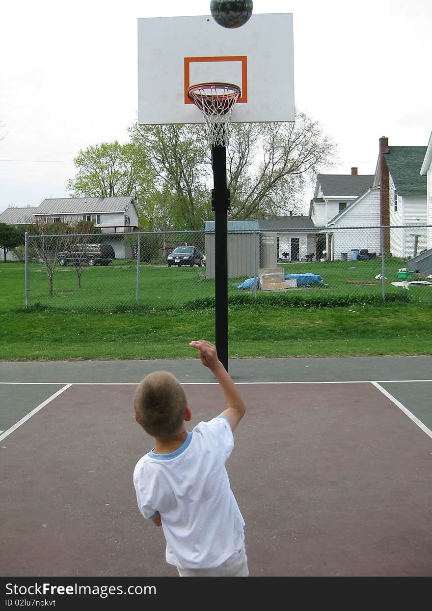 A young boy shoots hoops. He enjoys it and gets exercise. A young boy shoots hoops. He enjoys it and gets exercise.