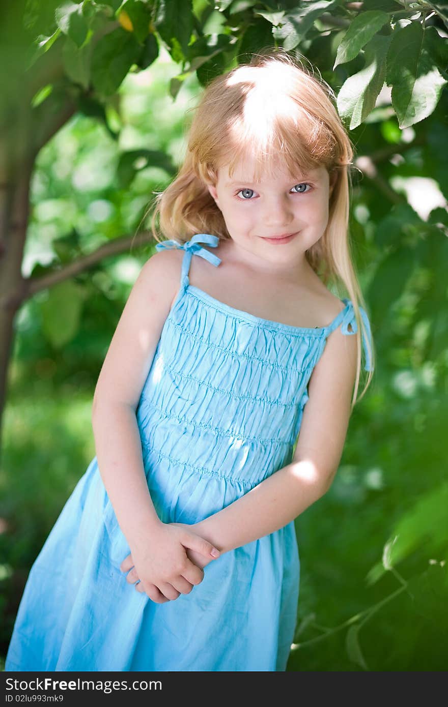 Little girl wearing blue dress in the park under trees