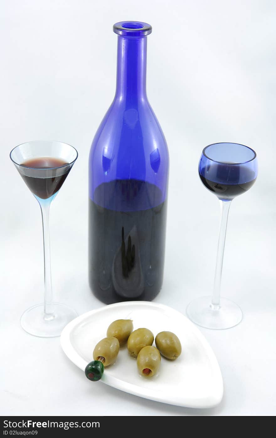 Blue cherry brandy bottle, two glasses and bunch of olives on the plate. Blue cherry brandy bottle, two glasses and bunch of olives on the plate.