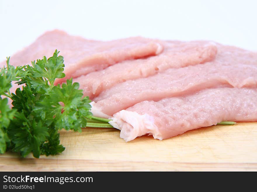 Raw tenderized pork chops on a chopping board decorated with parsley on white background
