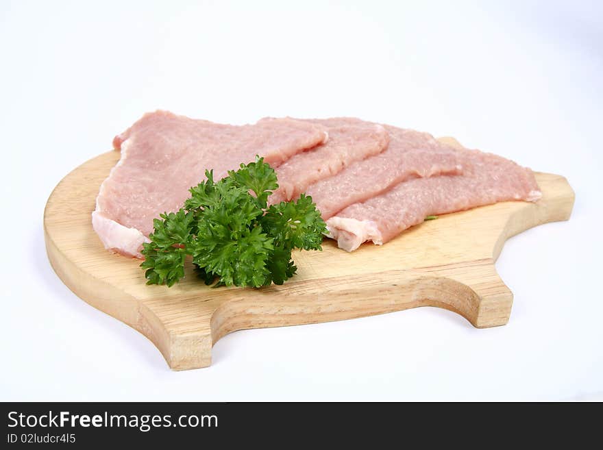 Raw tenderized pork chops on a pig shaped chopping board decorated with parsley on white background