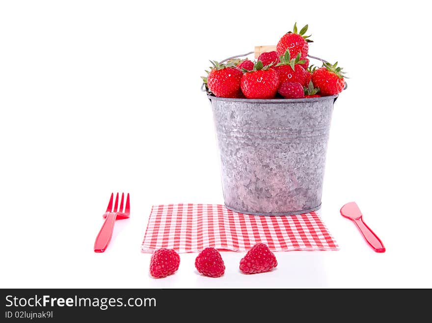 Cutlery with a bucket full of red fruit and a napkin isolated over white