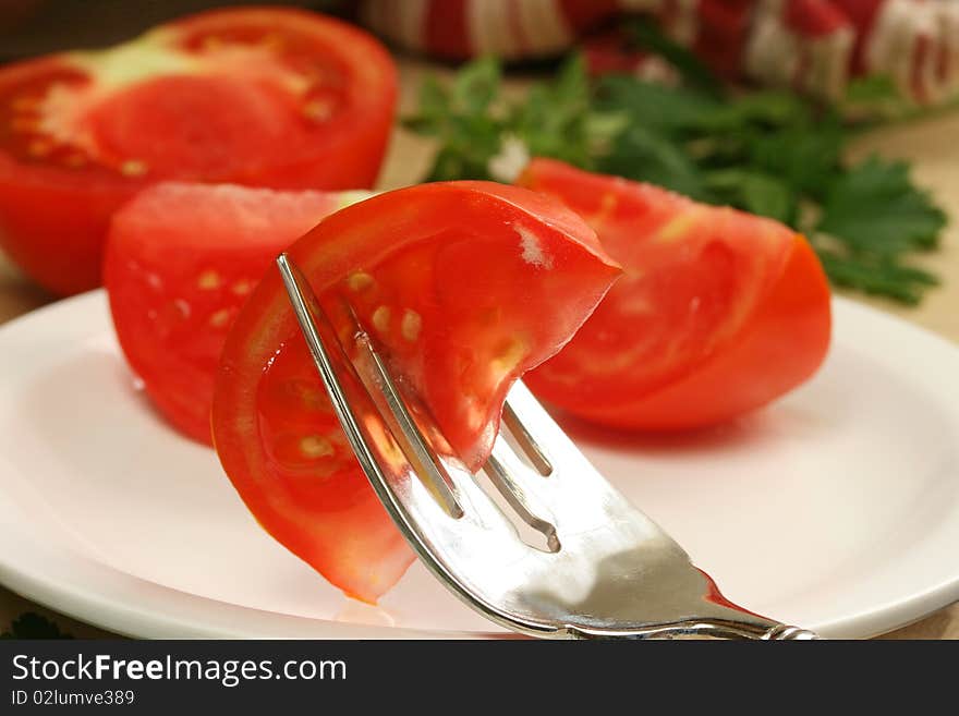 Tomato wedge on salad fork with tomaotes and herbs in background. Tomato wedge on salad fork with tomaotes and herbs in background.