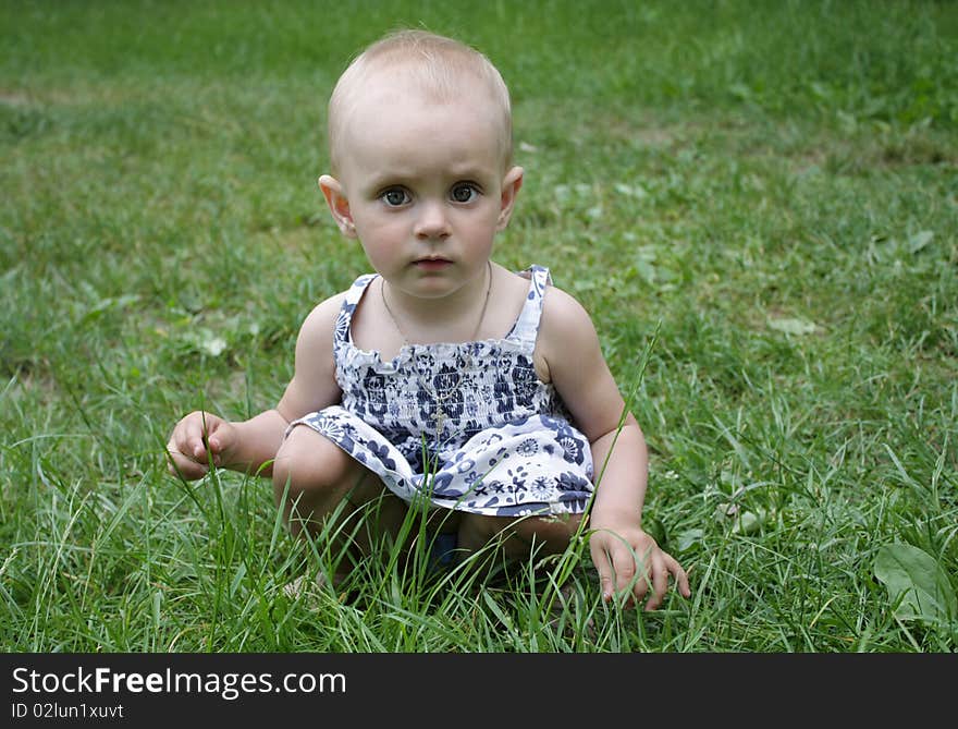 Small-eyed girl sitting in the green grass. Small-eyed girl sitting in the green grass