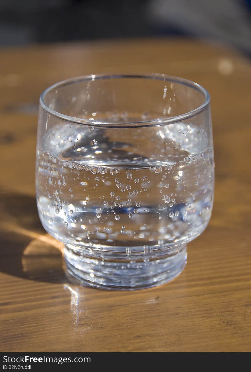 Close-up of a glass of sparkling mineral water on a wooden table in natural light. Close-up of a glass of sparkling mineral water on a wooden table in natural light.