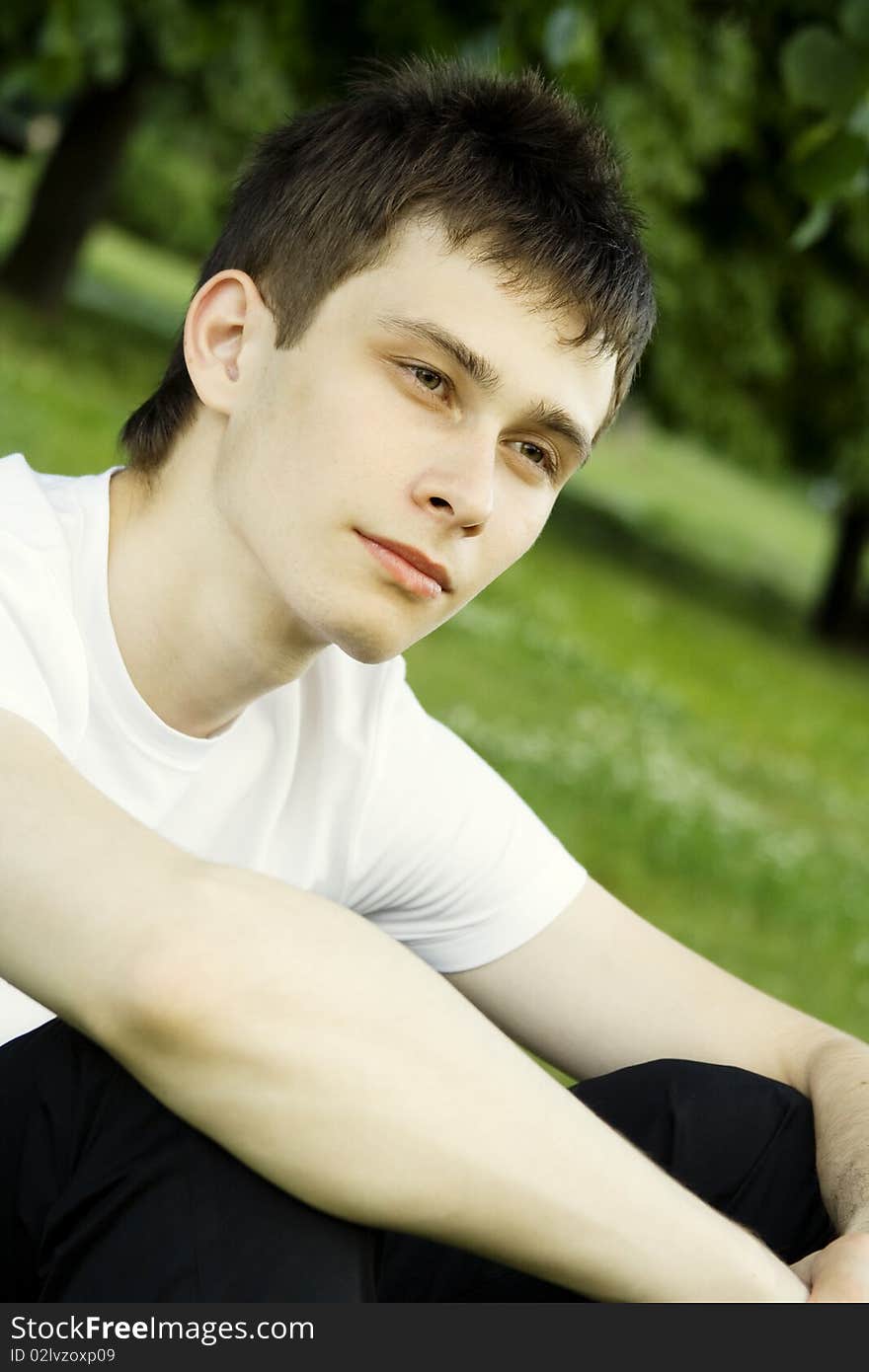 Teenager in a park in a white shirt against the green leaves of the tree. Teenager in a park in a white shirt against the green leaves of the tree