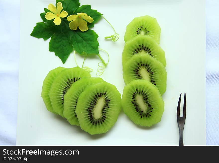 Kiwi slide on white plate background yellow flowers. Kiwi slide on white plate background yellow flowers