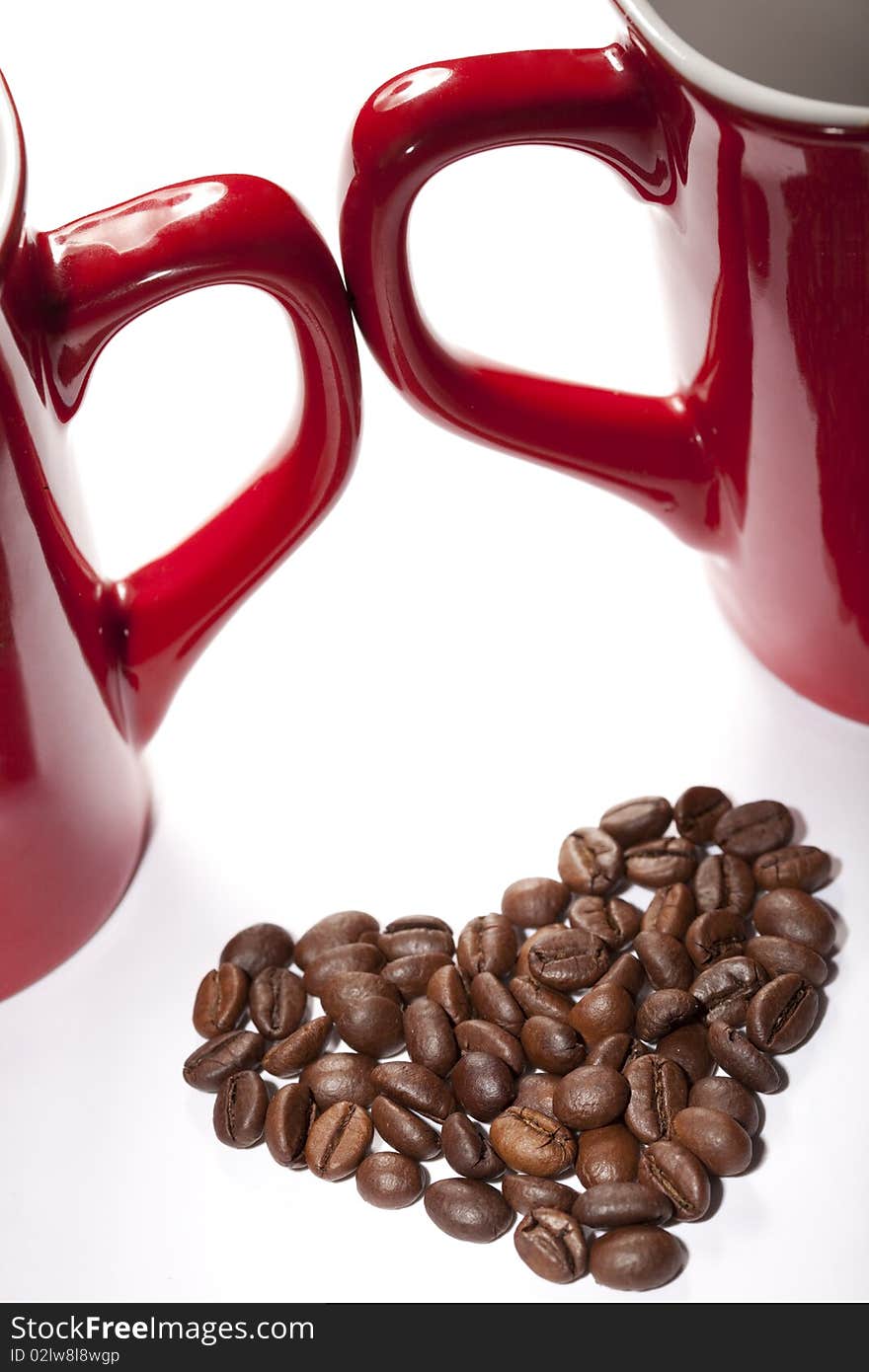 Coffee-beans heart against red cup`s handles on white backround