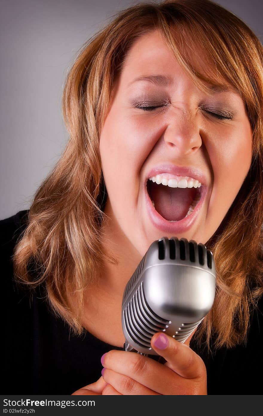 A beautiful young redheaded woman sings a song into an old fashion microphone. A beautiful young redheaded woman sings a song into an old fashion microphone.