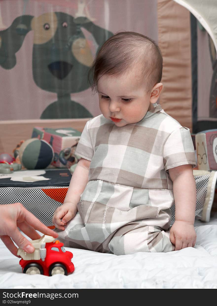 Year-old boy sitting on his knees and looks at a toy car. Year-old boy sitting on his knees and looks at a toy car