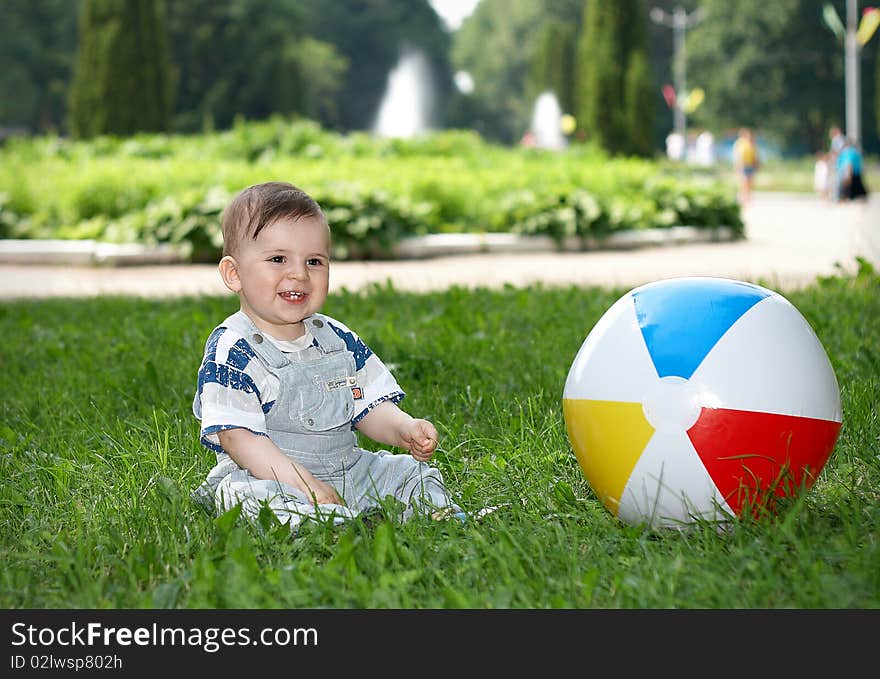 Little boy sitting on grass in the city park, beside the boy is colored ball. Little boy sitting on grass in the city park, beside the boy is colored ball