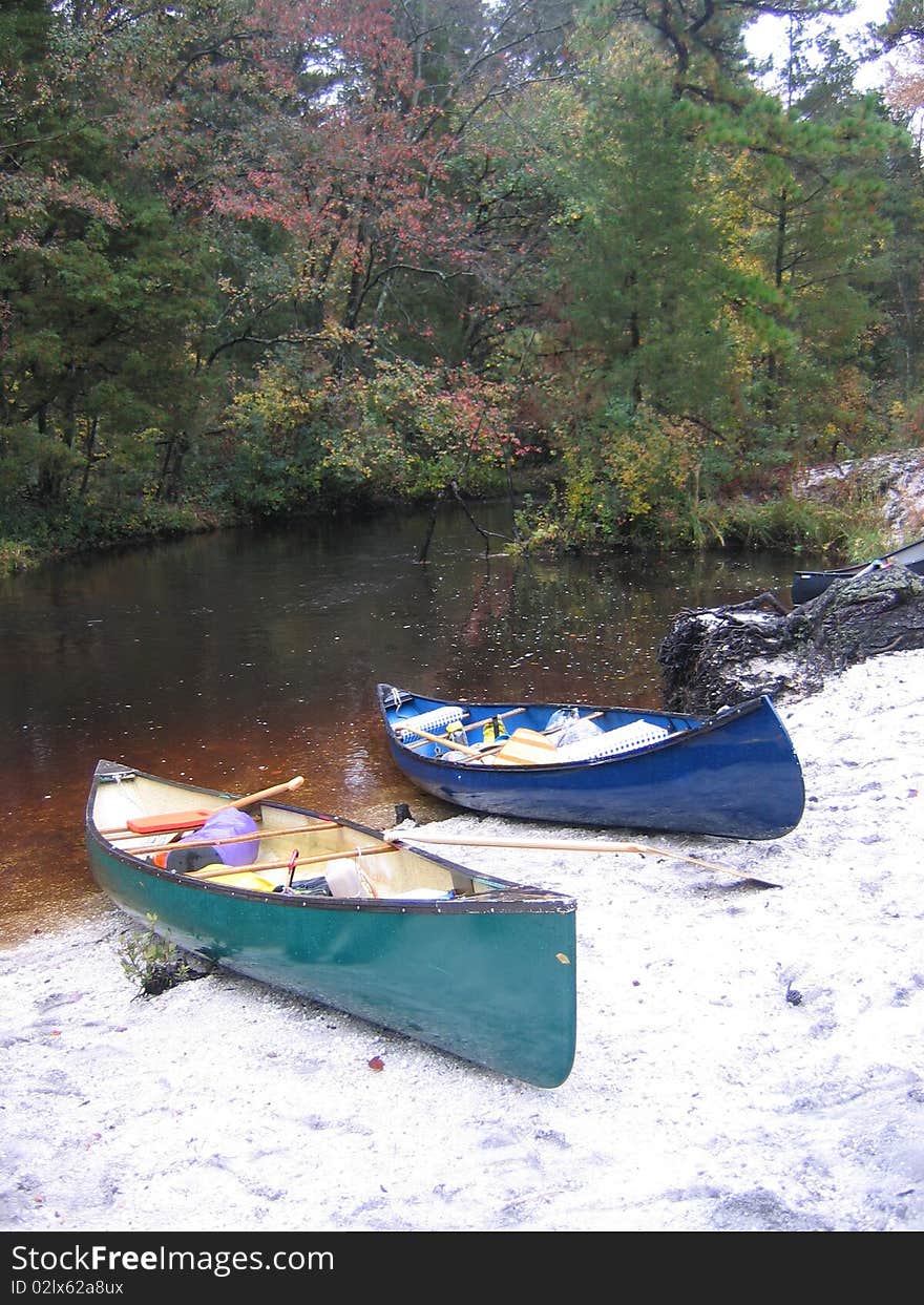 A blue and green canoe sit on river bank waiting to complete the journey. A blue and green canoe sit on river bank waiting to complete the journey