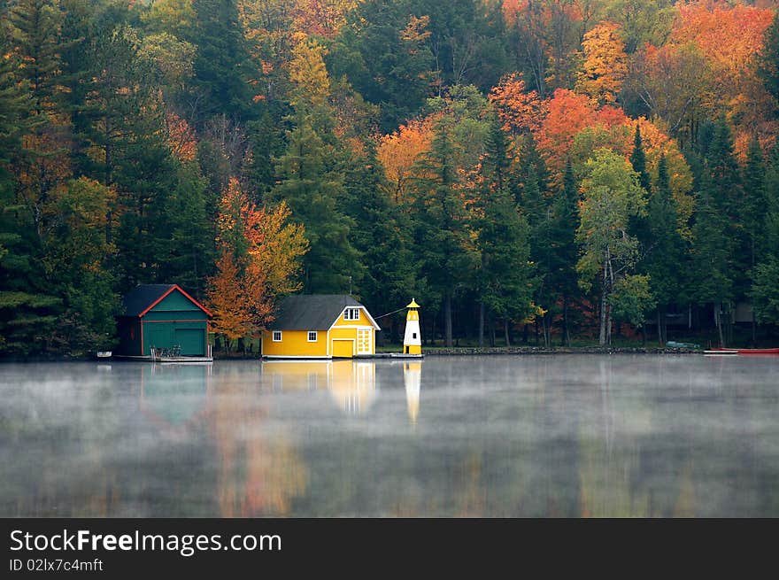 Yellow boathouse appears on early morning misty autumn lake