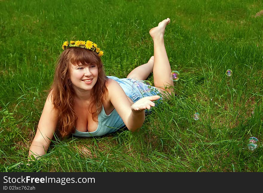 Portrait of a beautiful female with a dandelions garland, it is summer and she is playing with soap bubbles