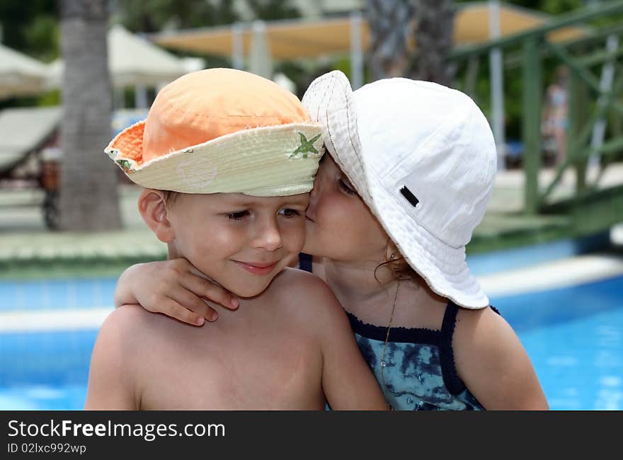 Little girl kissing a boy, on pool background