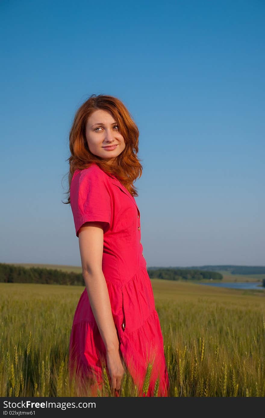 Redhead woman in red dress at wheat field sunset