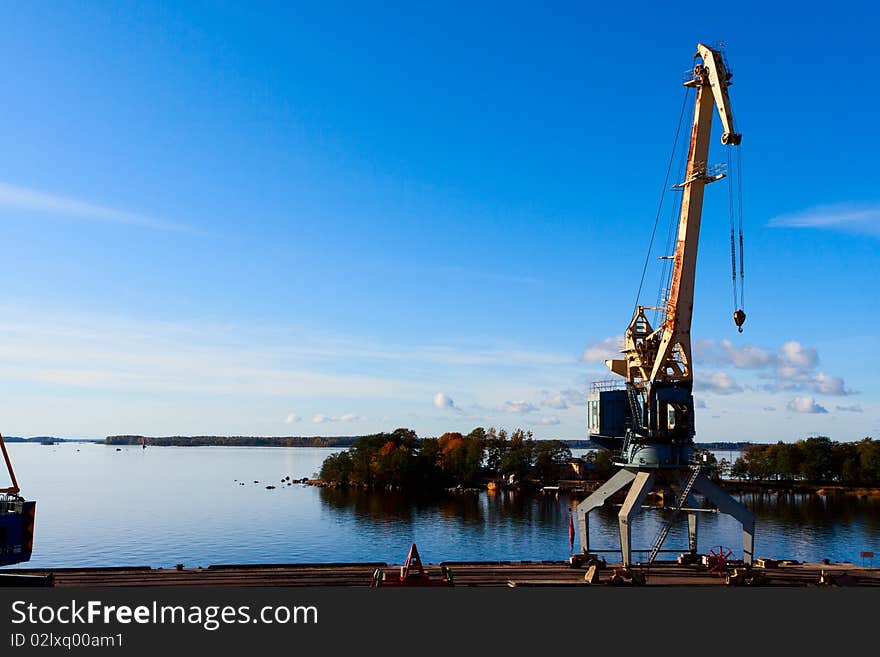 Sea port cranes with blue cloudy sky in background and water in foreground