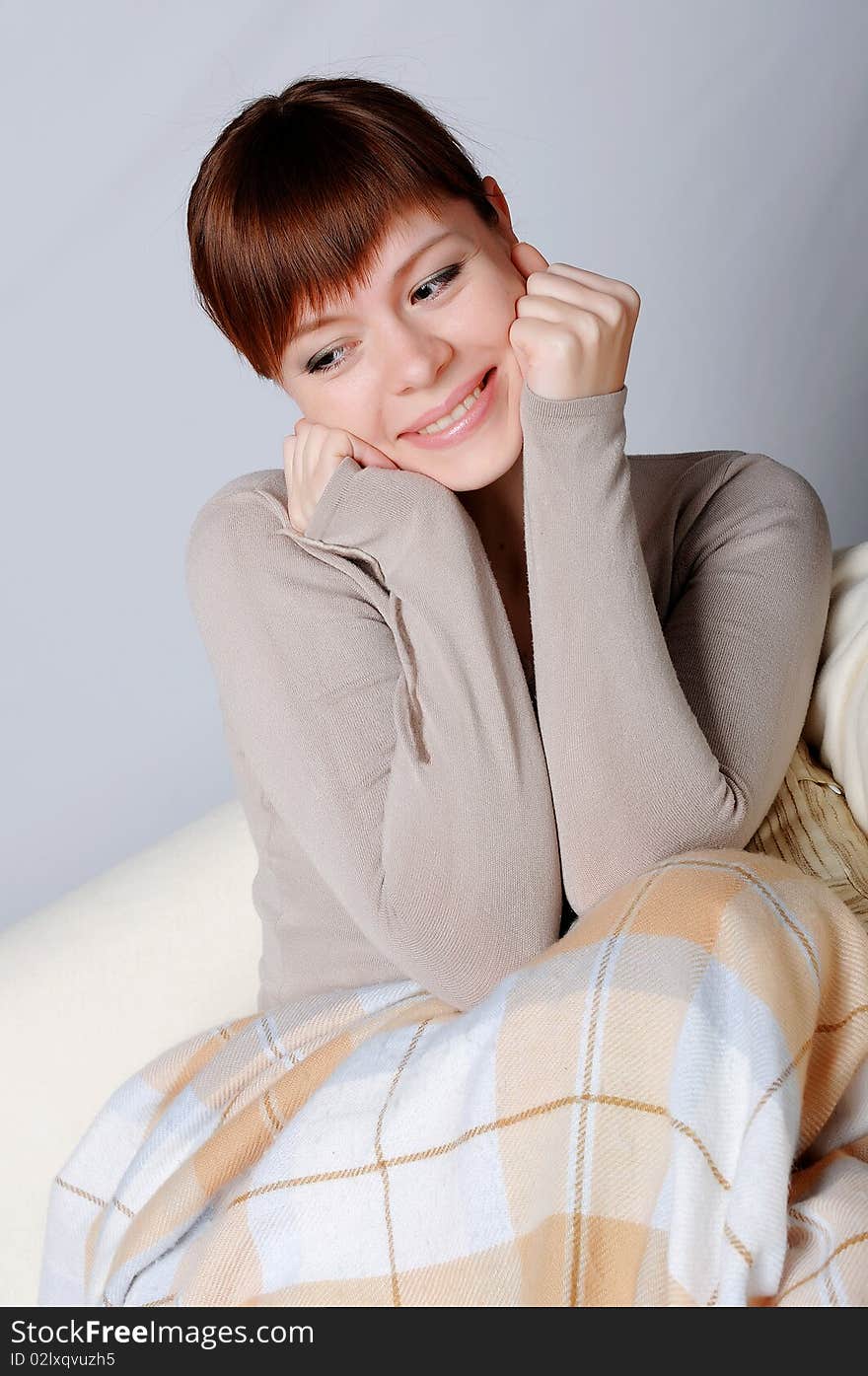 Young charming brunette in a gray jacket resting on the sofa