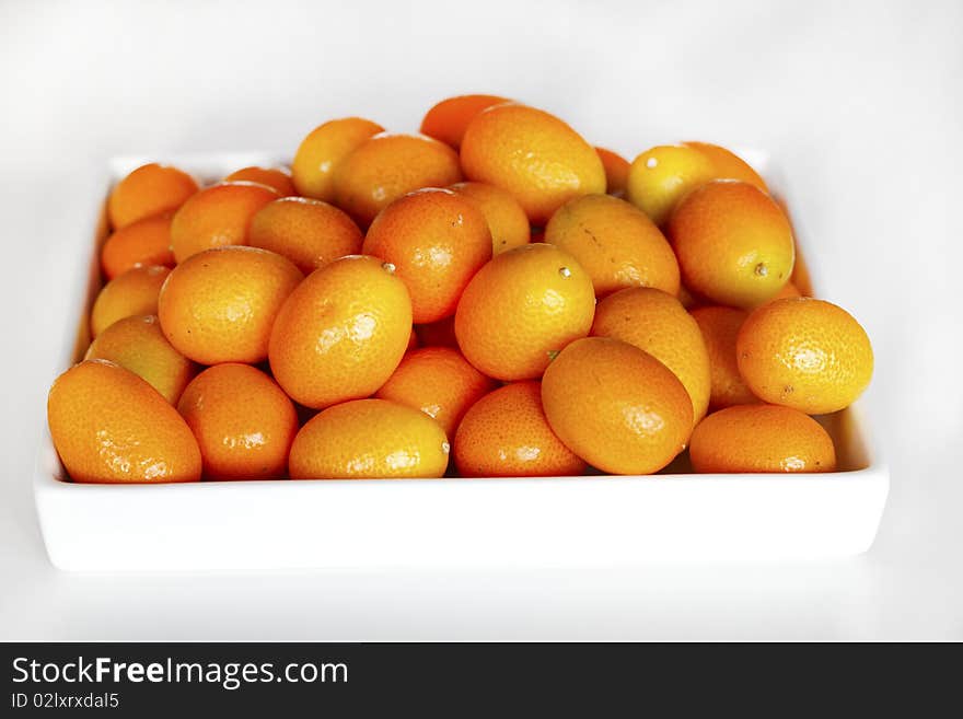 Kumquats piled on a white ceramic tray.