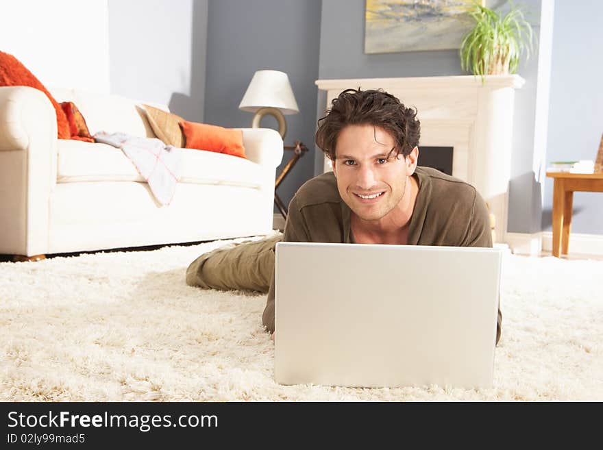 Man Using Laptop Relaxing Sitting On Rug At Home Smiling At Camera