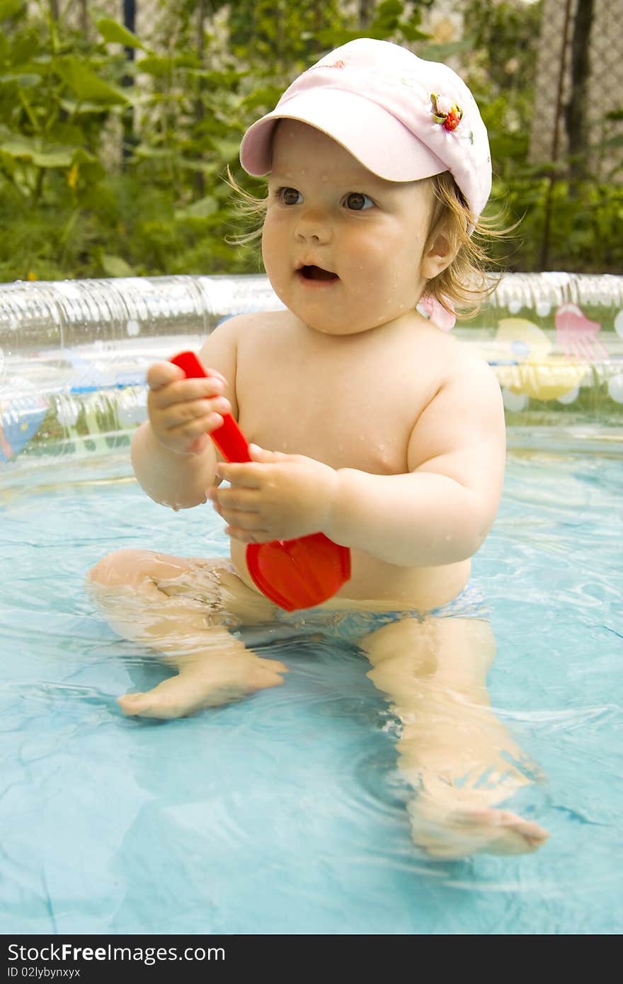 The surprised child with an open mouth in a cap with the big eyes sits in pool. The surprised child with an open mouth in a cap with the big eyes sits in pool