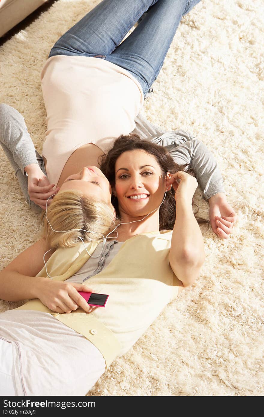 Two Women Listening To MP3 Player On Headphones Together Relaxing Laying On Rug At Home