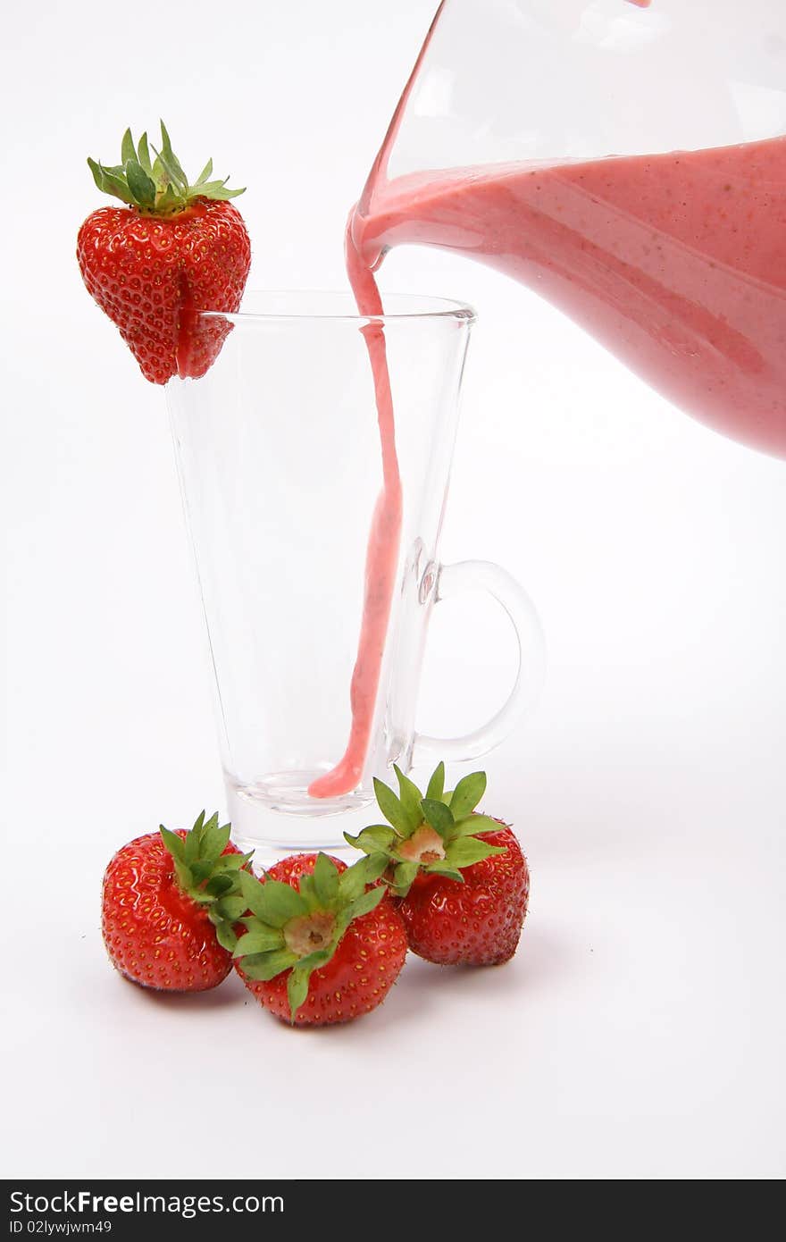 Strawberry shake being poured into a glass from a jug and some strawberries on white background