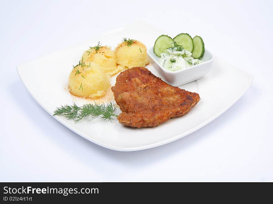 Pork chop (covered in batter and breadcrumbs), mashed potatoes and cucumber salad decorated with dill and parsley on a plate on white background. Pork chop (covered in batter and breadcrumbs), mashed potatoes and cucumber salad decorated with dill and parsley on a plate on white background