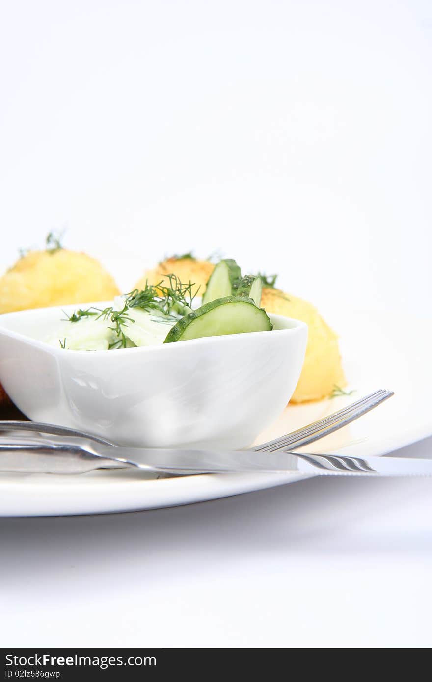 Cucumber salad in a bowl, with potatoes and a fork and a knife, on a plate, in close up