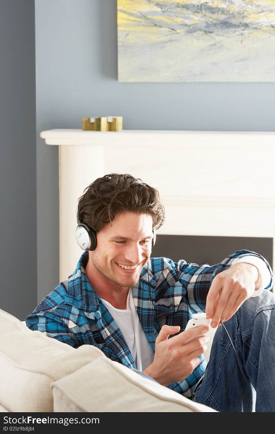 Man Listening To MP3 Player On Headphones Relaxing Sitting On Sofa At Home