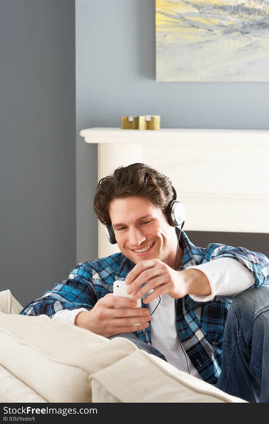 Man Listening To MP3 Player On Headphones Relaxing Sitting On Sofa At Home. Man Listening To MP3 Player On Headphones Relaxing Sitting On Sofa At Home