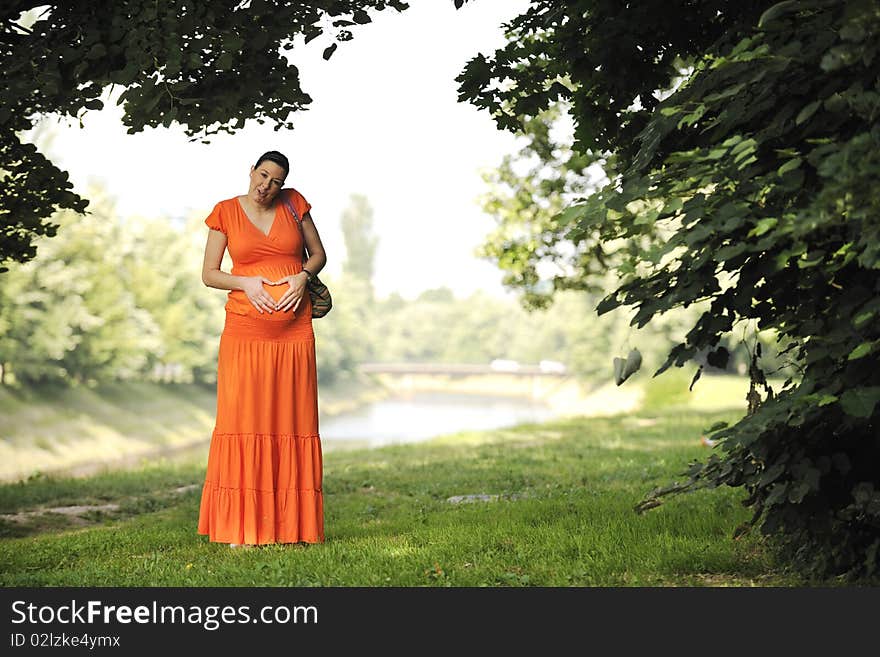 Beautiful young happy pregnant woman outdoor in bright nature in orange dress. Beautiful young happy pregnant woman outdoor in bright nature in orange dress