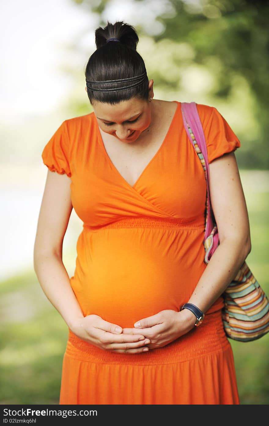 Beautiful young happy pregnant woman outdoor in bright nature in orange dress. Beautiful young happy pregnant woman outdoor in bright nature in orange dress