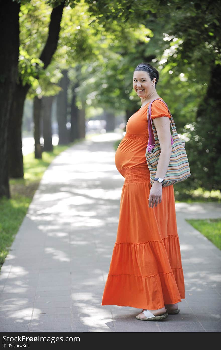 Beautiful young happy pregnant woman outdoor in bright nature in orange dress. Beautiful young happy pregnant woman outdoor in bright nature in orange dress