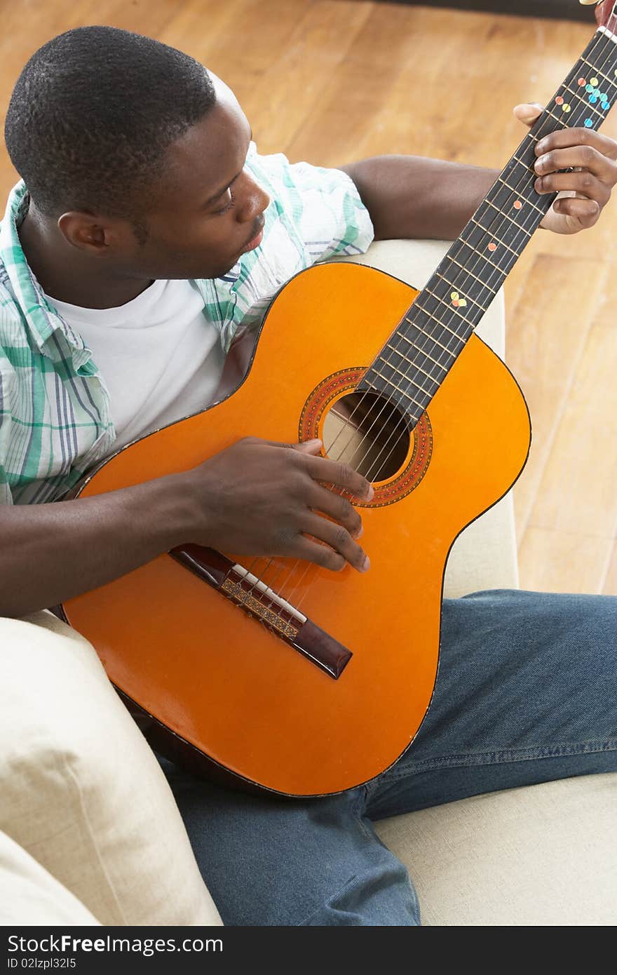 Young Man Relaxing Sitting On Sofa Playing Acoustic Guitar. Young Man Relaxing Sitting On Sofa Playing Acoustic Guitar