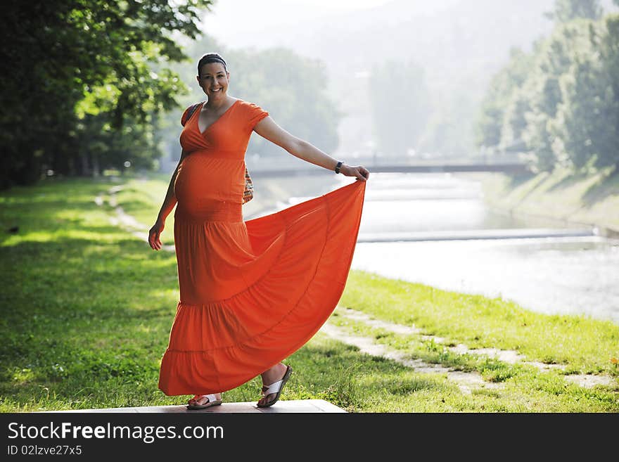 Beautiful young happy pregnant woman outdoor in bright nature in orange dress. Beautiful young happy pregnant woman outdoor in bright nature in orange dress