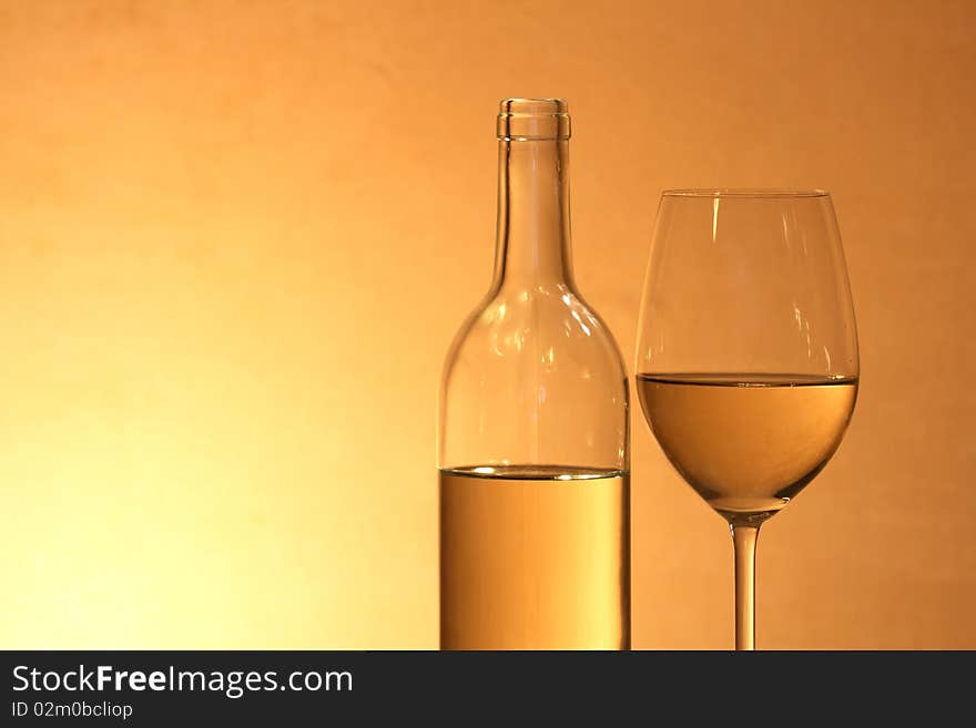 Wineglass near bottle of white wine with reverberation on red-yellow background