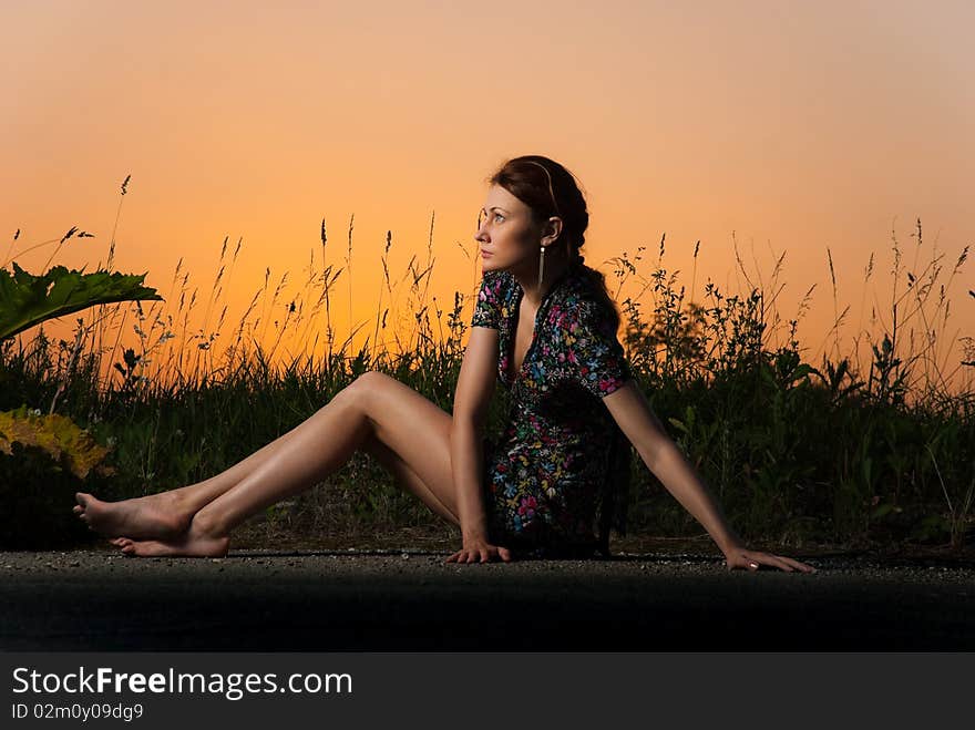 Young redhead woman sitting at summer roadside sunset. Young redhead woman sitting at summer roadside sunset