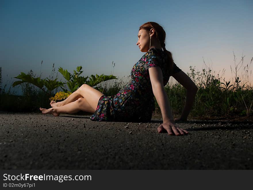 Young redhead woman sitting at summer roadside sunset. Young redhead woman sitting at summer roadside sunset