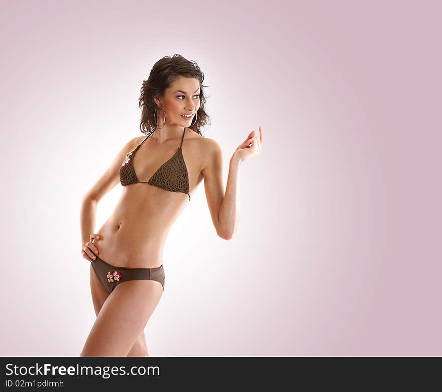 A young and sexy brunette is posing in a brown swimsuit. Image isolated on a light purple gradient background. A young and sexy brunette is posing in a brown swimsuit. Image isolated on a light purple gradient background.