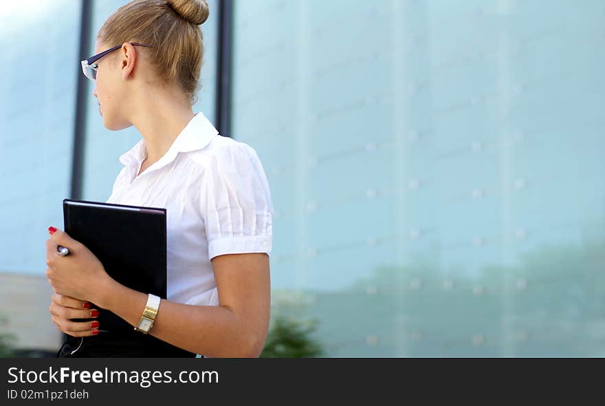 A young and attracitve business woman in formal clothes is standing with a notebook. Image taken on a modern street background. A young and attracitve business woman in formal clothes is standing with a notebook. Image taken on a modern street background.