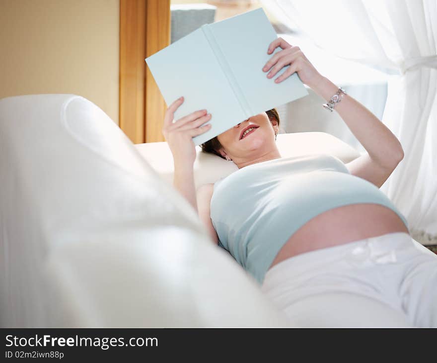 Italian 7 months pregnant woman lying down on sofa and reading book. Horizontal shape, high angle view, Copy space. Italian 7 months pregnant woman lying down on sofa and reading book. Horizontal shape, high angle view, Copy space