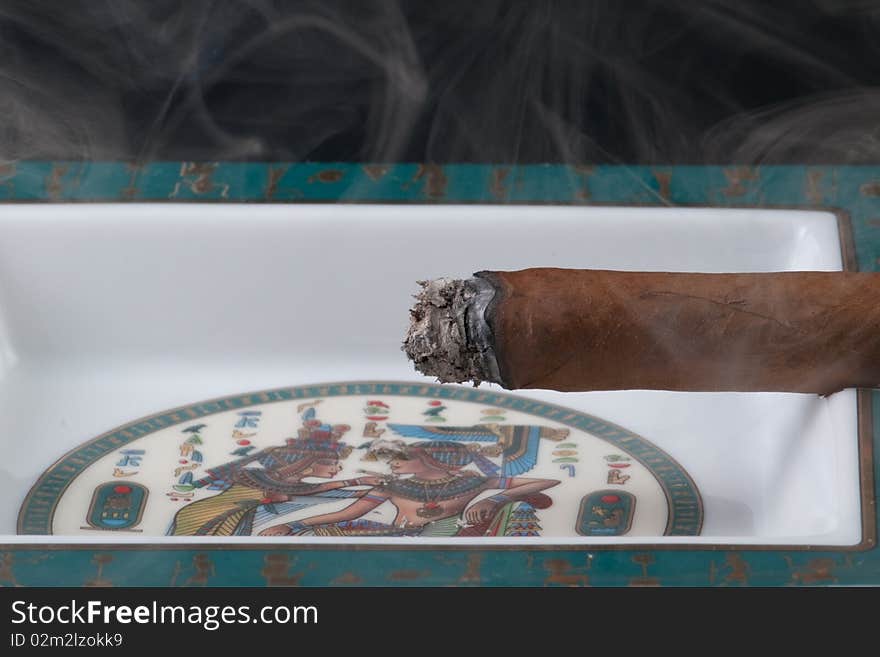 A cigar with curling smoke resting in an ashtray. A cigar with curling smoke resting in an ashtray